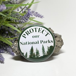 May include: A green button with white text that reads "PROTECT our NATIONAL PARKS". The button features a silhouette of a forest with green trees.