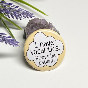 May include: A yellow button with a white speech bubble that says "I have vocal tics. Please be patient."