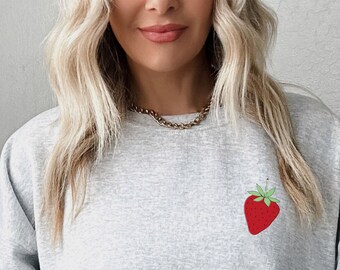 Könnte beinhalten: Ein grauer Pullover mit einem kleinen roten Erdbeermotiv auf der Vorderseite.