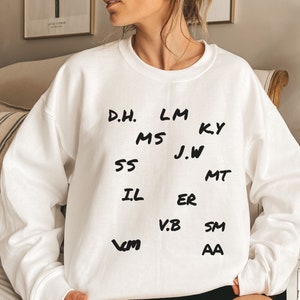 May include: White sweatshirt with black handwritten text on the front. The text reads: "D.H. LM KY MS J.W SS IL ER V.B SM VM AA"