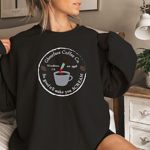 May include: Black sweatshirt with a white circle graphic featuring a coffee cup with a bloody knife sticking out of it. The text around the graphic reads "Ghostface Coffee Co. Woodboro, CA est. 1996 So good it'll make you SCREAM"