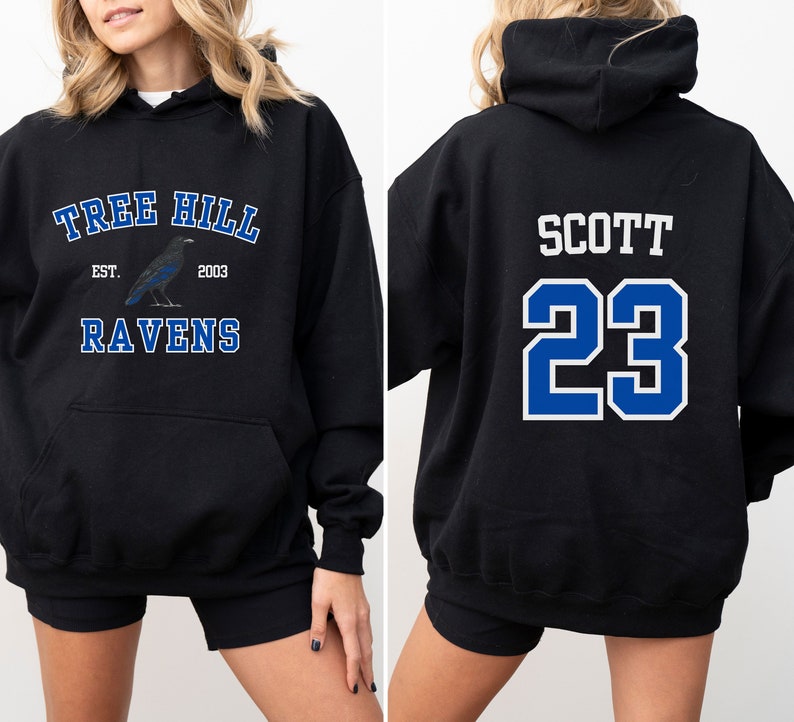 Op de afbeelding: Zwart hoodie met een blauwe en witte afbeelding aan de voorkant met de tekst "Tree Hill Est. 2003 Ravens" en een blauwe en witte afbeelding aan de achterkant met de tekst "Scott 23".