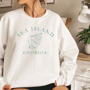 May include: White sweatshirt with a blue graphic of a seashell and the text "SEA ISLAND GEORGIA".