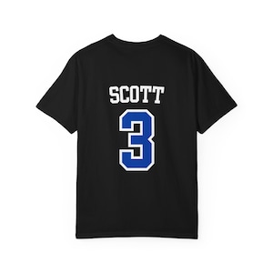 以下が含まれることがあります： 背面に白いブロック体でSCOTTという名前と、白い縁取りが施された大きな青い数字の3がプリントされた黒い半袖Tシャツ。この衣類はクルーネックで、スポーツジャージのような標準的なフィット感のデザインです。