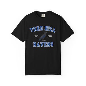 May include: A black short-sleeved t-shirt featuring a graphic print with the text "TREE HILL" in blue arched letters above a black raven illustration, with "EST. 2003" in white and the word "RAVENS" in blue block letters at the bottom.