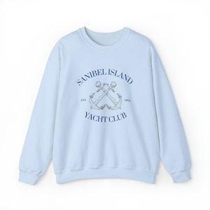 May include: Light blue sweatshirt with a navy blue graphic of two crossed anchors and the text "Sanibel Island Yacht Club Est. 1954".