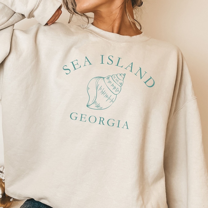 May include: A beige sweatshirt with a teal graphic of a seashell and the text "SEA ISLAND GEORGIA".