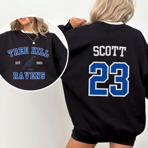May include: Black sweatshirt with a blue and white design on the back. The design includes the name "SCOTT" and the number "23". The front of the sweatshirt has a blue and white design with the text "TREE HILL EST. 2003 RAVENS" and a black raven.