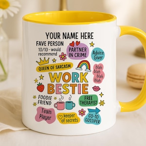 May include: White ceramic mug with a yellow interior and handle. The mug features the text "YOUR NAME HERE" and "WORK BESTIE" with various other phrases and icons. A vase of daisies and two macarons are in the background.