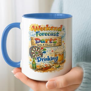 May include: A white ceramic mug with a blue handle and interior rim. The front features a colourful graphic with the text "Weekend Forecast Darts With A Chance Of Drinking," a dartboard, darts, a beer mug, a green bottle, and a brown bottle.