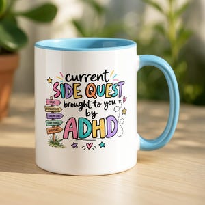 May include: A white ceramic mug with a light blue handle and rim. The front features colourful text reading current SIDE QUEST brought to you by ADHD, accompanied by a wooden signpost graphic labelled with ideas, distractions, random stuff, shiny things, and adventures.