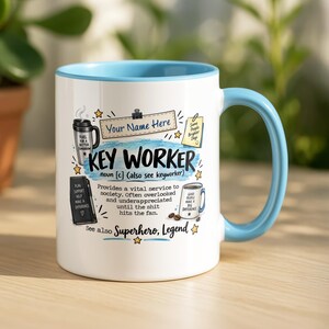 May include: A white ceramic mug with a light blue handle and rim. The design features the text "KEY WORKER" with a dictionary-style definition, illustrations of a travel mug, a notebook, and a coffee mug, plus the text "Your Name Here".