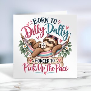 May include: A square greeting card featuring a brown sloth wearing pink sunglasses, relaxing in a colourful hammock while holding a white mug labelled No Rush. The text reads BORN TO Dilly Dally FORCED TO Pick Up The Pace with pink hearts and flowers.