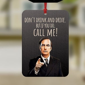 May include: A black and white car air freshener with a picture of a man in a suit and tie. The text on the air freshener reads "Don't drink and drive. But if you do, call me!"