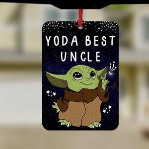 Könnte beinhalten: Ein Auto-Lufterfrischer mit einer grünen Alienfigur, die einen leuchtenden Stock hält. Der Text auf dem Lufterfrischer lautet "Yoda Best Uncle".