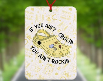 May include: Yellow car air freshener with a white background and the text "If you ain't crocin you ain't rockin". The air freshener features a yellow cartoon clog with various charms.