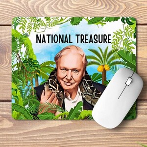 May include: A mouse mat featuring a cartoon illustration of a man with a snake wrapped around his shoulders. The background is a jungle scene with palm trees and lush foliage. The text "NATIONAL TREASURE" is printed in black at the top of the mouse mat.