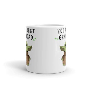 May include: White ceramic mug with a green and brown cartoon character on each side. The text on the left side reads "The Best Dad" and the text on the right side reads "Yoda Best Grandad".