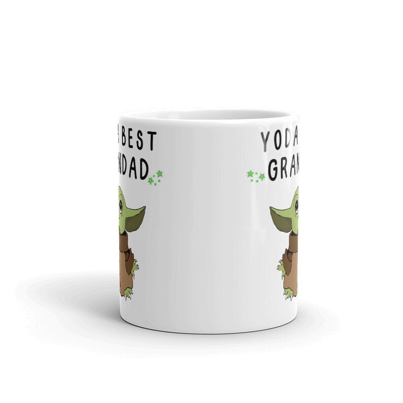 May include: White ceramic mug with a green and brown cartoon character on each side. The text on the left side reads "The Best Dad" and the text on the right side reads "Yoda Best Grandad".