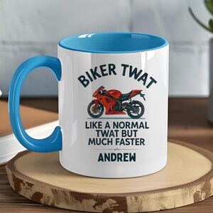 May include: White ceramic mug with a blue interior and handle. The mug features the text "BIKER TWAT" above a red motorcycle illustration. Below the illustration, the text reads "LIKE A NORMAL TWAT BUT MUCH FASTER" and "ANDREW".