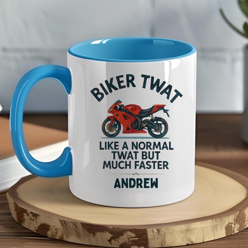 May include: White ceramic mug with a blue interior and handle. The mug features the text "BIKER TWAT" above a red motorcycle illustration. Below the illustration, the text reads "LIKE A NORMAL TWAT BUT MUCH FASTER" and "ANDREW".