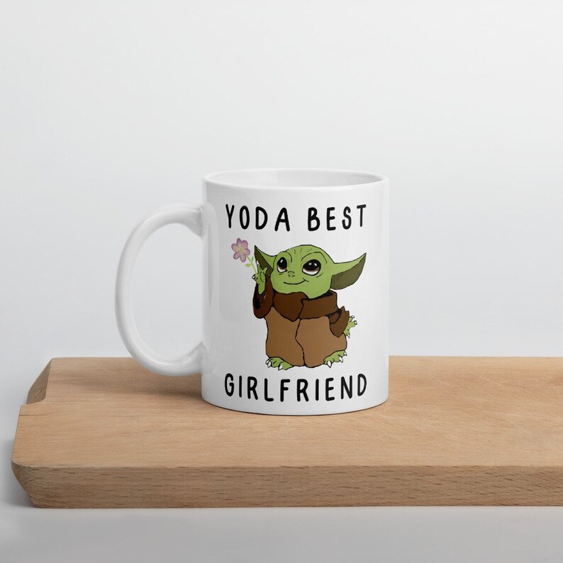 May include: White ceramic mug with a green cartoon character holding a flower. The text "YODA BEST GIRLFRIEND" is printed on the mug.