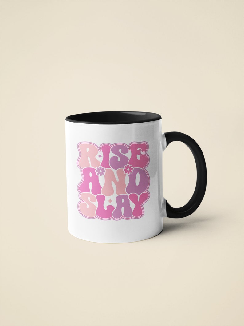May include: White ceramic mug with a black rim and handle. The mug features a pink and purple graphic that says "Rise and Slay" in a retro font.