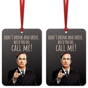 May include: Two black rectangular car air fresheners with a white background and a picture of a man in a suit. The text on the air fresheners reads "Don't drink and drive. But if you do, call me!"
