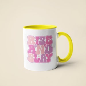 May include: White ceramic mug with a yellow rim and handle. The mug features a pink and purple graphic that says "Rise and Slay" in a retro font.