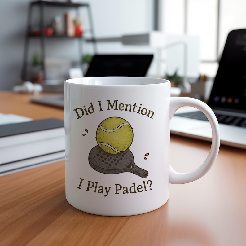 May include: White ceramic mug with the text "Did I Mention I Play Padel?" featuring a yellow tennis ball and a padel racket illustration. The mug is on a wooden surface.
