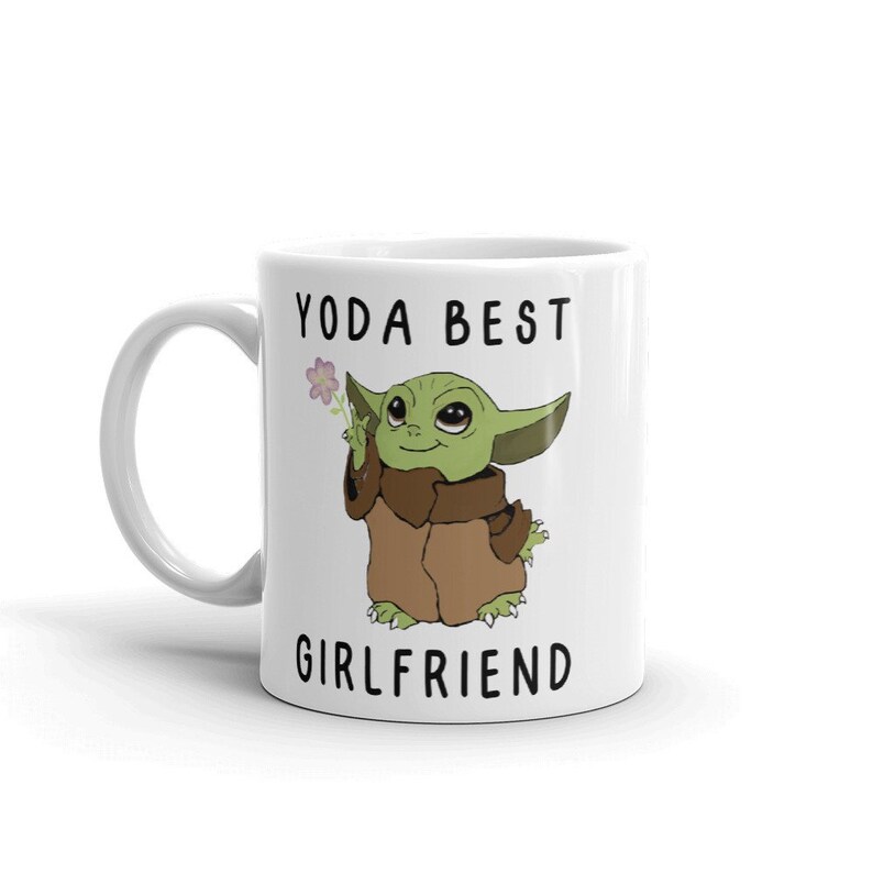 May include: White ceramic mug with a green cartoon character holding a flower. The text "YODA BEST GIRLFRIEND" is printed on the mug.