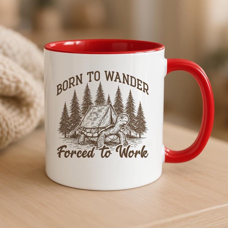May include: White ceramic mug with a red interior and handle. The mug features a graphic of a turtle with a tent and trees, and the text "Born to Wander, Forced to Work" in brown.