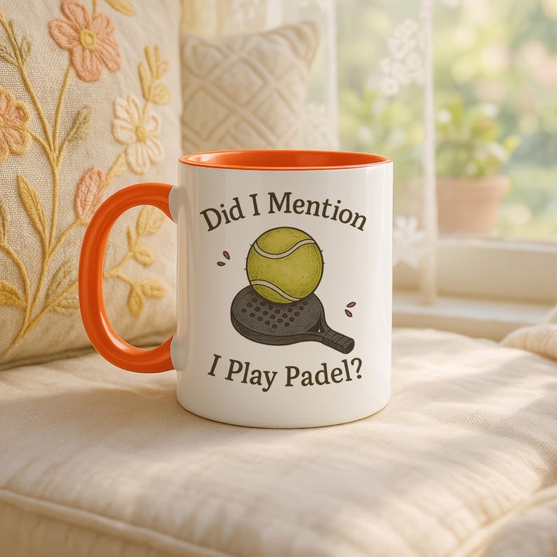 May include: White ceramic mug with an orange handle and interior. The mug features the text "Did I Mention I Play Padel?" along with a graphic of a padel ball and racket. The mug is set against a soft, neutral background.