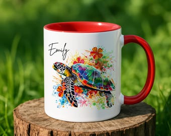 Może przedstawiać: Biały ceramiczny kubek z czerwonym wnętrzem i uchwytem. Kubek zdobi kolorowy wzór żółwia morskiego z kwiatowymi akcentami i imieniem "Emily" w skrypcie. Kubek stoi na drewnianej powierzchni.
