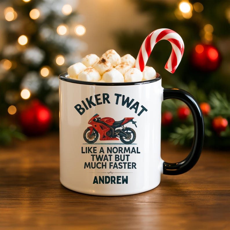May include: White ceramic mug with a black handle and rim, filled with marshmallows and a candy cane. The mug features the text "BIKER TWAT" above a red motorcycle graphic, with additional text below. The name "ANDREW" is printed at the bottom.