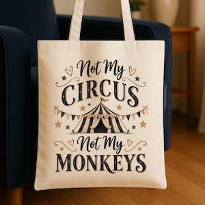 Peut inclure: Un sac fourre-tout en toile couleur crème avec un motif noir et doré représentant un chapiteau de cirque. Le texte indique Not My CIRCUS Not My MONKEYS. Le design comprend des étoiles, des cœurs et des fanions décoratifs autour du chapiteau.