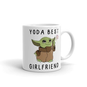 May include: White ceramic mug with a green cartoon character holding a flower. The text "YODA BEST GIRLFRIEND" is printed on the mug.