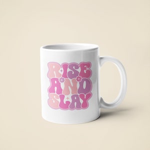 May include: White ceramic mug with a pink, purple, and white graphic that says "Rise and Slay" in a retro font.