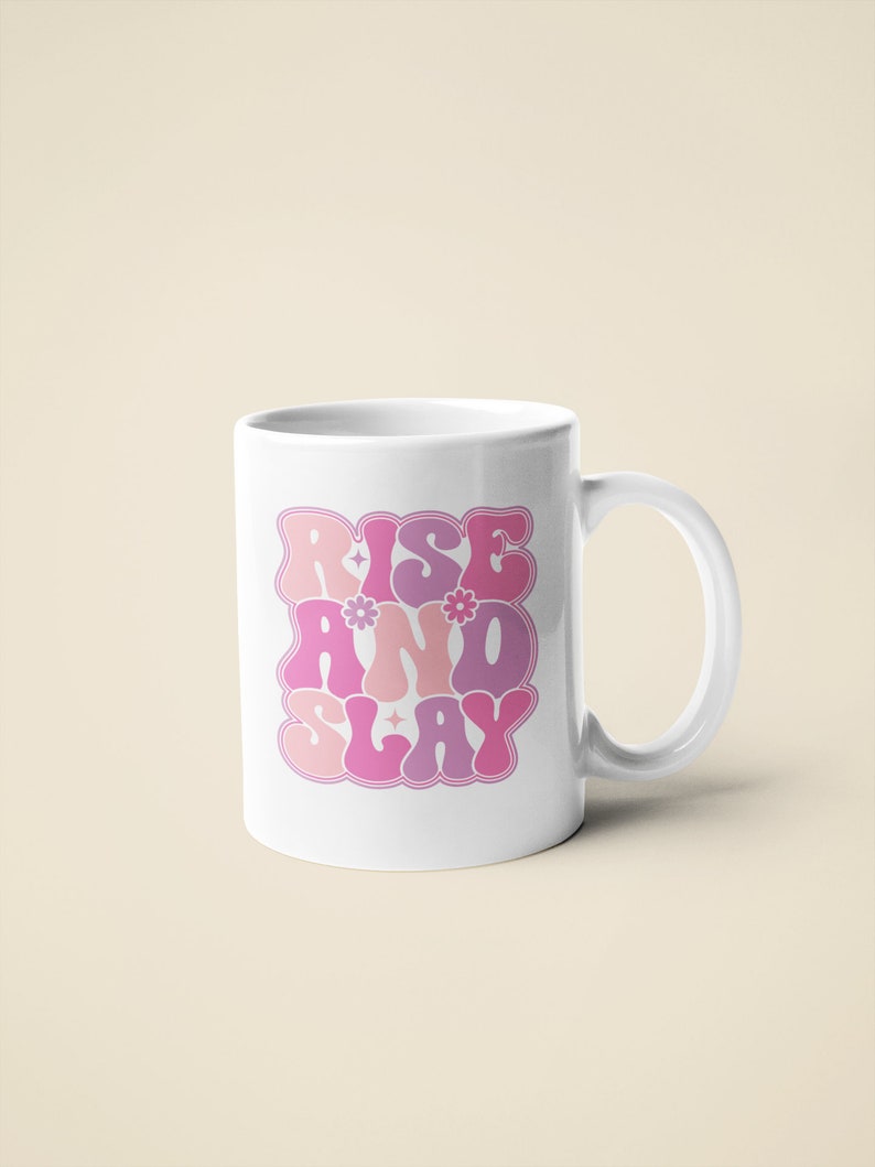 May include: White ceramic mug with a pink, purple, and white graphic that says "Rise and Slay" in a retro font.