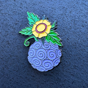 May include: A purple and blue swirl design enamel pin with a yellow flower on top. The flower has a red center and green leaves.