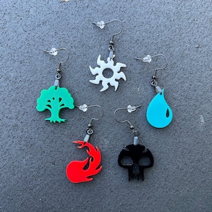 May include: Five pairs of earrings with different colored symbols. The symbols are a white sun, a green tree, a blue teardrop, a red flame, and a black skull.