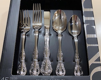 May include: A boxed set of Oneida Michelangelo silverware. The set includes forks, knives, and spoons with ornate, detailed handles. The box is black with the Oneida logo and the name "Michelangelo". The set is described as a 45-piece set, service for 8.