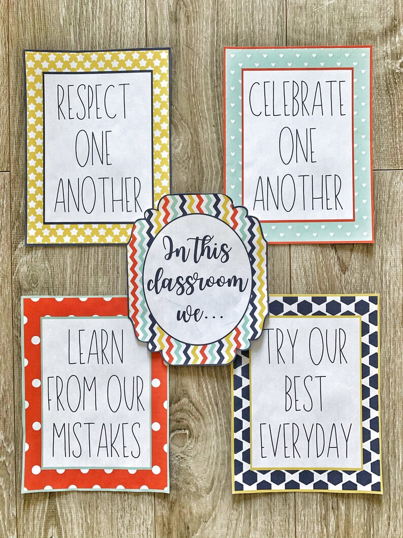 May include: Five colorful classroom posters with positive messages. The posters have decorative borders and include phrases like "Respect One Another," "Celebrate One Another," "Learn From Our Mistakes," and "Try Our Best Everyday." A central sign reads "In this classroom we..."