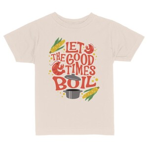 May include: A beige t-shirt with a red, yellow, and green graphic design. The graphic features a pot, corn, and crawfish with the text "Let the good times boil."
