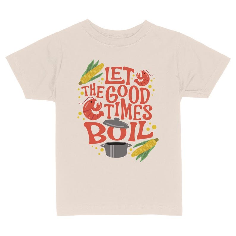 May include: A beige t-shirt with a red, yellow, and green graphic design. The graphic features a pot, corn, and crawfish with the text "Let the good times boil."