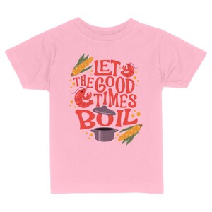May include: Pink kids' t-shirt with a graphic design of a pot, corn, and crawfish with the text "Let the good times boil."