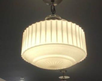 May include: Two white ceiling light fixtures with ribbed glass shades. The top fixture has a chain hanging from it. The bottom fixture is smaller and has a shorter chain.