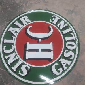May include: Circular Sinclair Gasoline sign with a green border and white lettering. The centre features a red circle with a white "HC" logo. The words "SINCLAIR GASOLINE" are written around the edge.