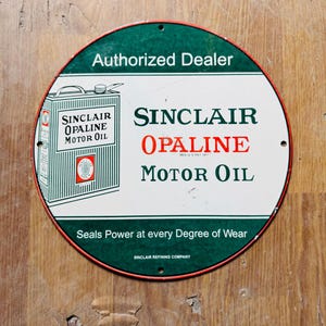 May include: A round, white and green sign with red trim advertising Sinclair Opaline Motor Oil. The sign features a vintage illustration of a can of motor oil and the text "Authorized Dealer", "Sinclair Opaline Motor Oil", "Seals Power at every Degree of Wear", and "Sinclair Refining Company".