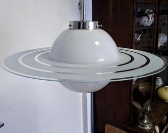 May include: A white glass ceiling light fixture with a chrome finish and a circular, layered glass shade. The shade has a white, frosted glass centre and a clear glass outer ring with three concentric circles.